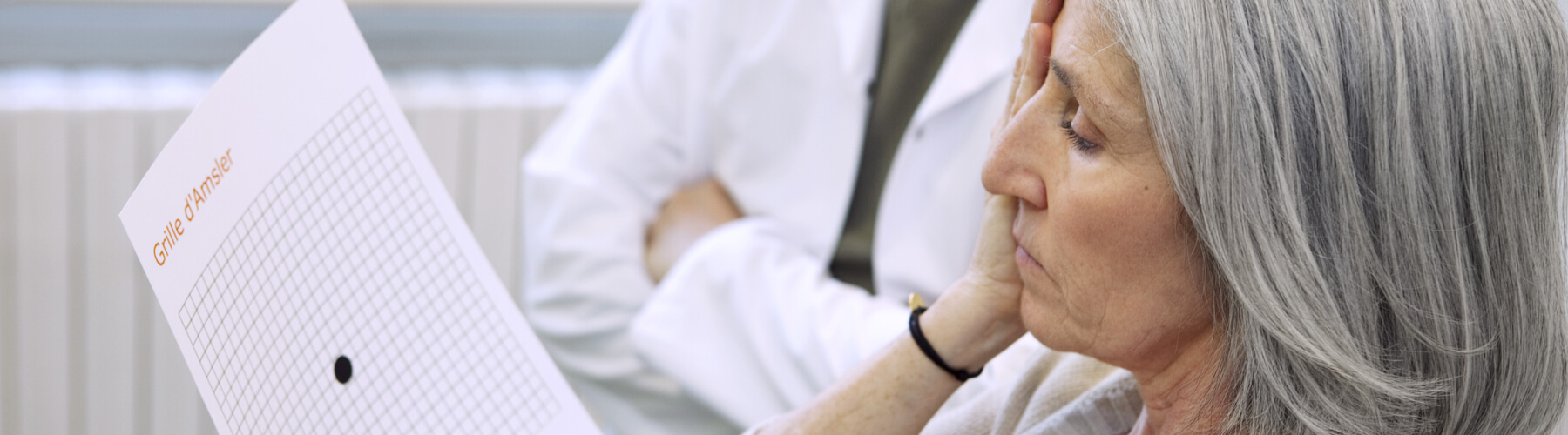 senior woman doing an age related macular degeneration or AMD screening, with an opthamologist in the background