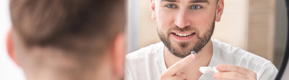 Close-up photograph of young man putting contact lens in eye 