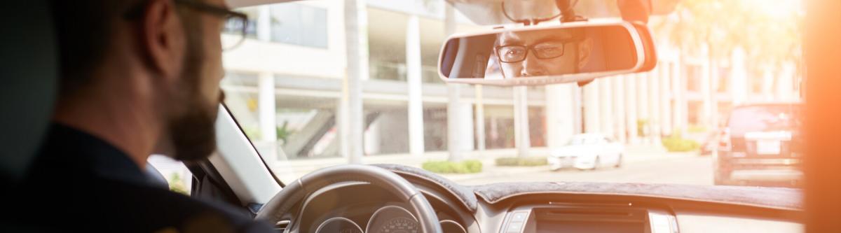 Young businessman driving to work, view over the shoulder, driving with glasses, vision screening or requirements for drivers license concept