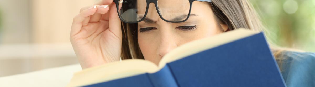 Nearsighted woman suffering eyestrain trying to read a book at home