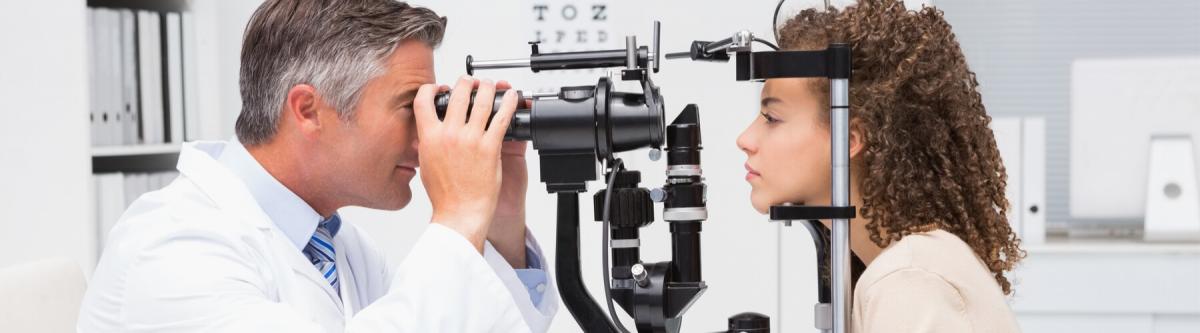 male optometrist giving an eye exam to a young female in exam room