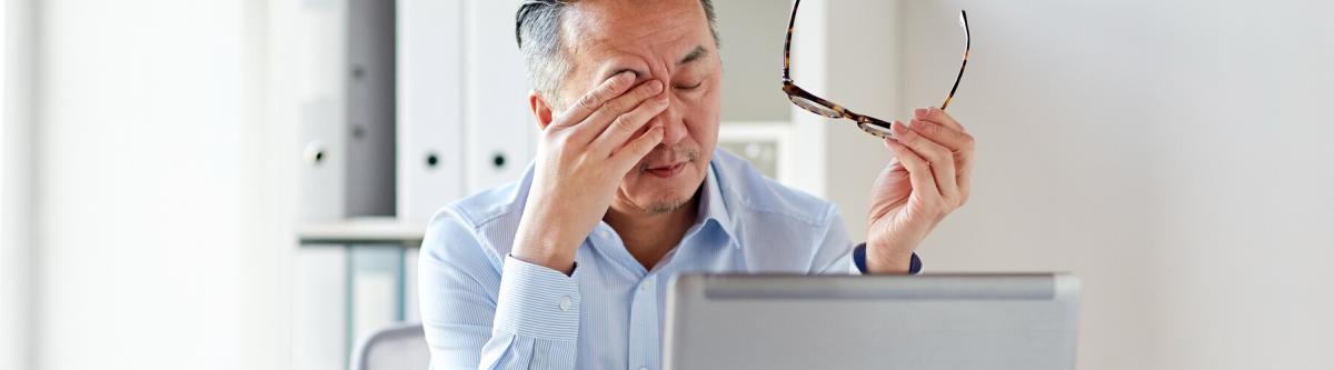 elderly asian man rubbing eyes and holding glasses while at the computer