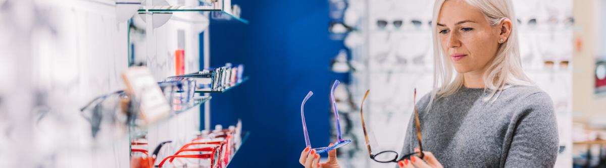 woman standing at display case with glasses, frames, choosing between them