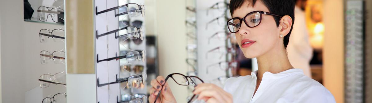 young adult woman in front of a display case with glasses, choosing glasses or frames